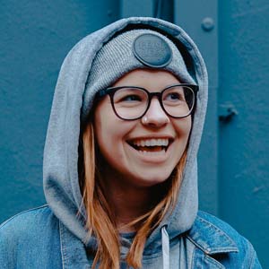 A young teen with red hair and black glasses in a hoodie smiling