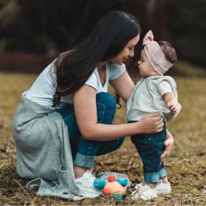 A young mother crouching down to hold her baby girl toodler