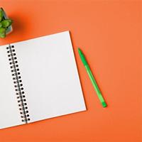 Open notebook and green pen on an orange background